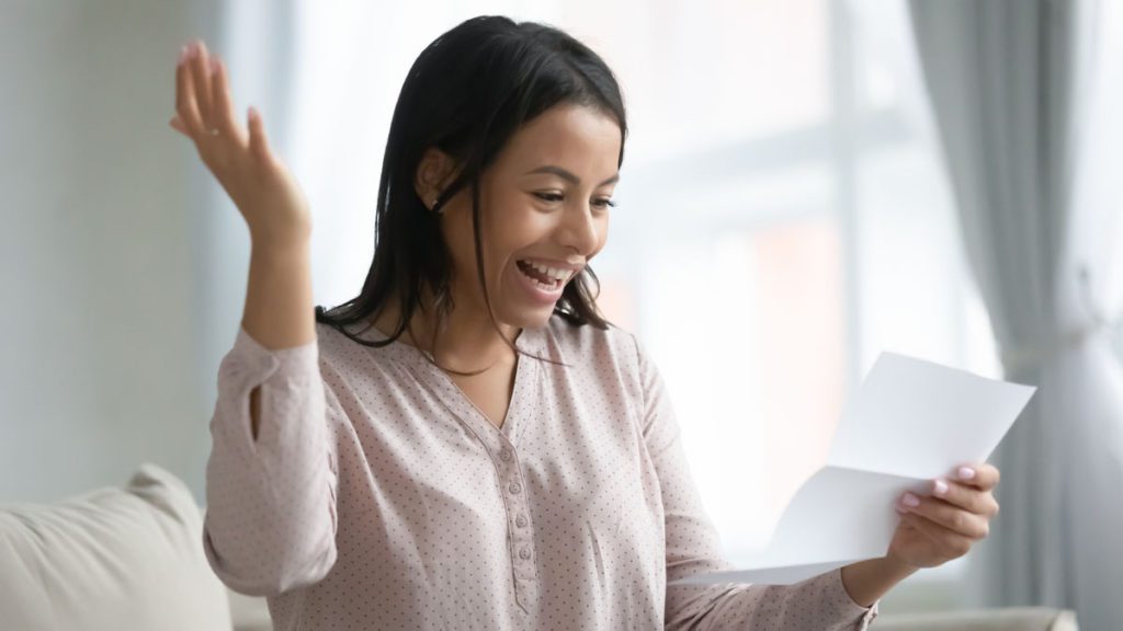 Lady excitedly looking at paper in hand with other arm in the air
