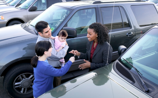 Saleswoman giving keys to new car to young family
