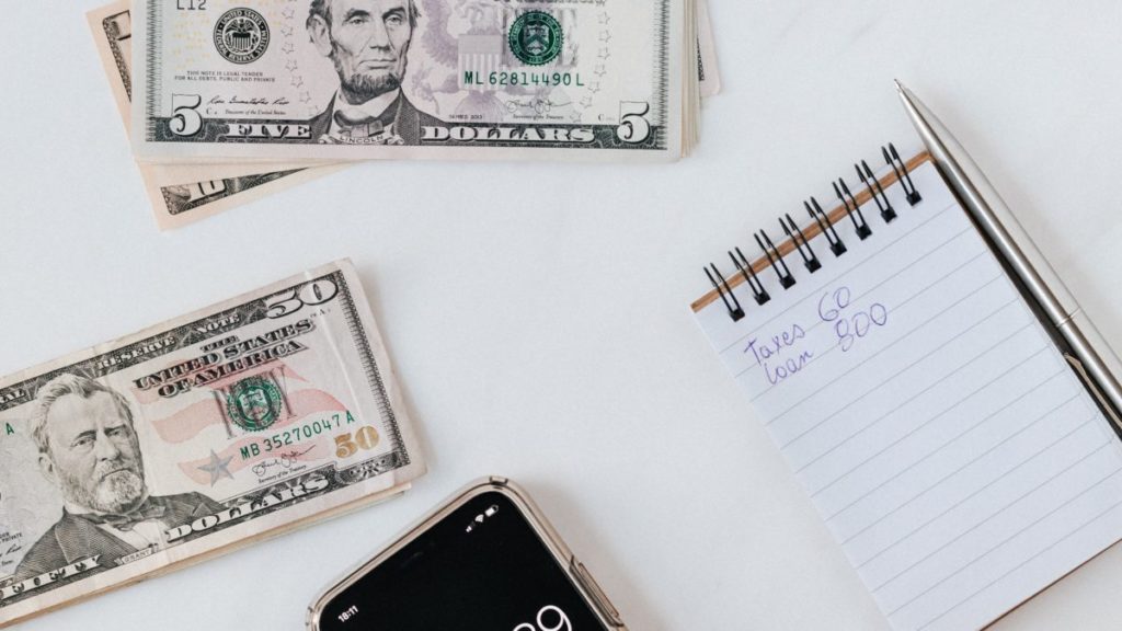 Dollar bills, calculator, and notebook sitting on flat surface