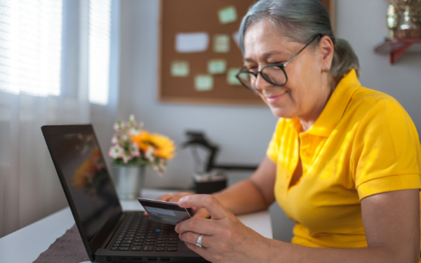 Older woman sitting at desk in office using credit card at laptop