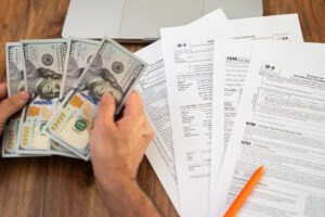 Person counting hundred-dollar bills while reviewing tax forms. Financial planning and tax preparation concept, ideal for tax season and accounting themes