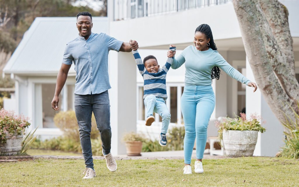 Happy parents lifting their kid by their new home in the outdoor garden while playing together. Backyard, bonding and African mother and father holding their boy child in the backyard of their house