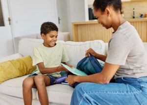 Mother helping son to get ready for school, helping him with backpack and books, hugging and leaving home
